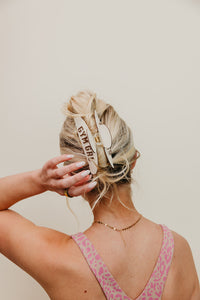 Person with styled hair wearing a cream and brown gym girl claw, against a beige background