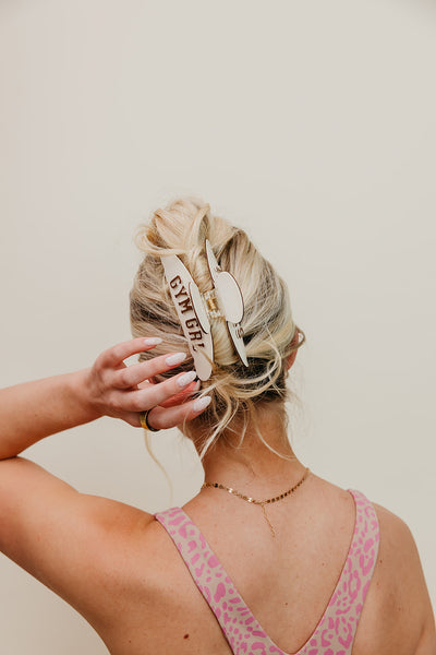 Person with styled hair wearing a cream and brown gym girl claw, against a beige background