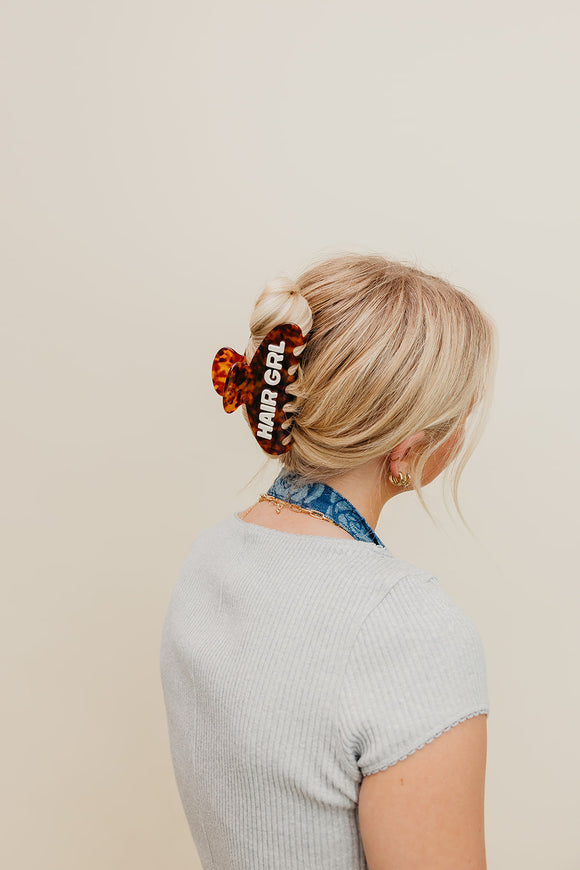 Person with a brown HAIR GRL claw in their hair on a beige background