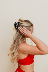 Person with blonde hair wearing a black and white gym girl claw, against a plain background