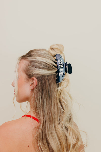 Woman with blonde hair tied back with a black hair clip against a beige background