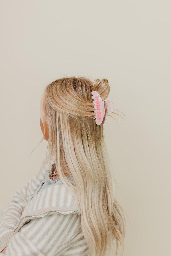 Person with long blonde hair wearing a pink HAIR GIRL claw on a beige background