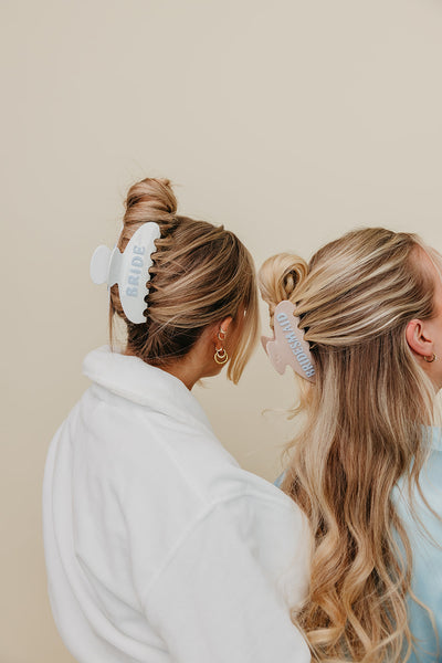 Two women with styled hair using hair bride and bridesmaid clips against a beige background
