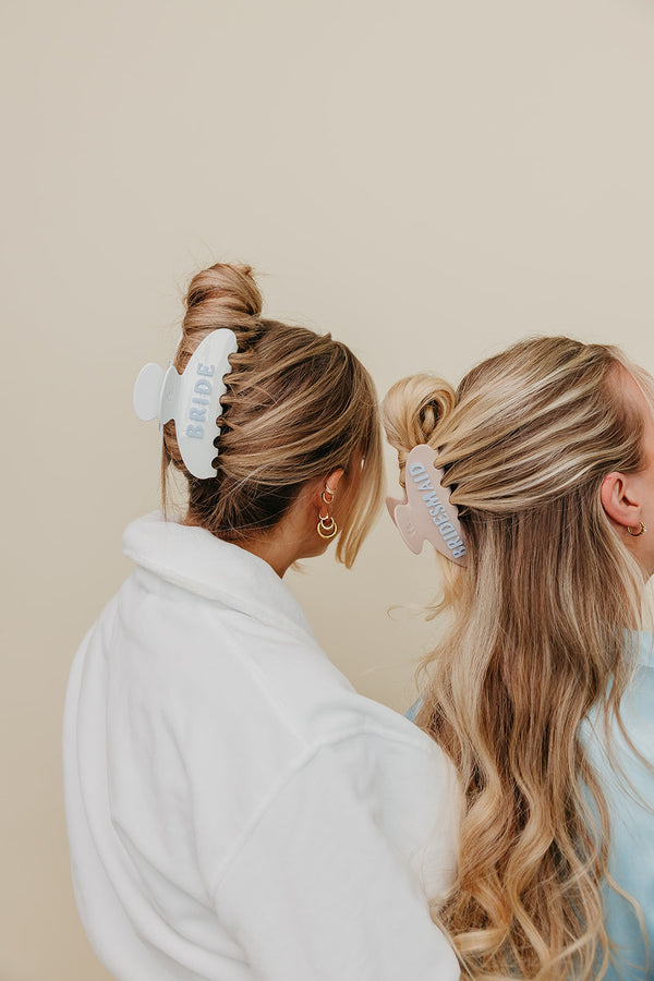Two women with styled hair using hair bride and bridesmaid clips against a beige background