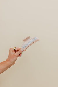 Hand holding a cream claw with blue bridesmaid lettering against a neutral background