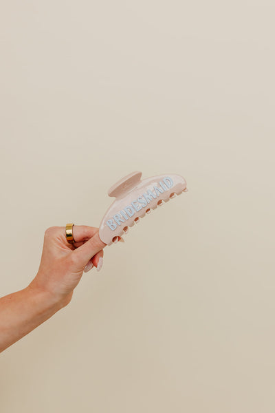 Hand holding a cream claw with blue bridesmaid lettering against a neutral background