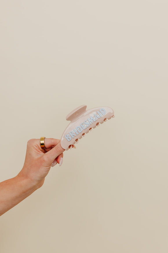 Hand holding a cream claw with blue bridesmaid lettering against a neutral background