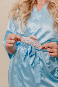 Person wearing a light blue robe holding a 'Bridesmaid' claw.