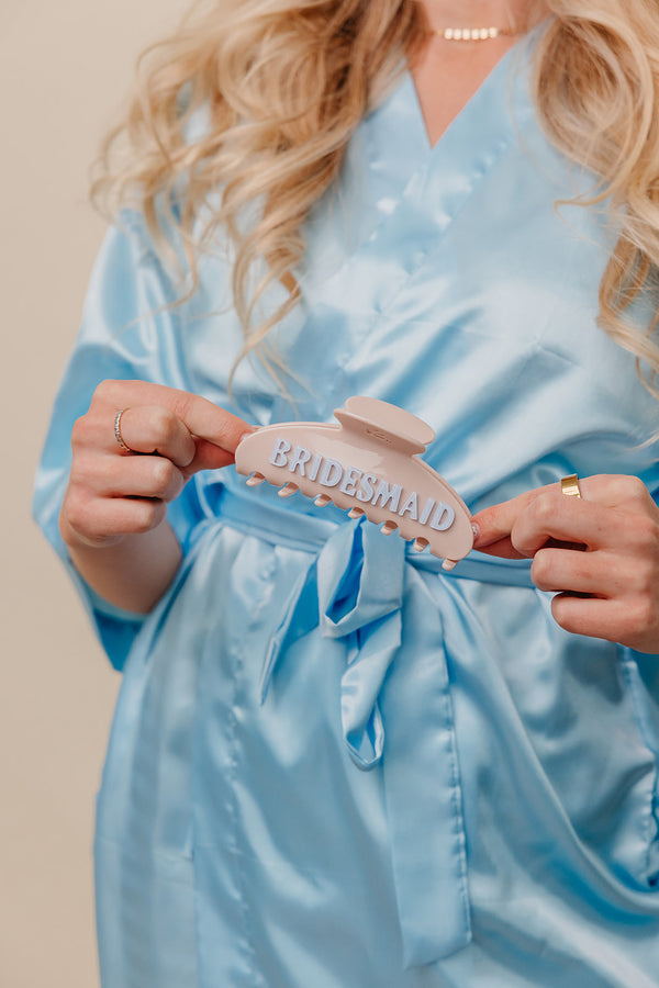 Person wearing a light blue robe holding a 'Bridesmaid' claw.