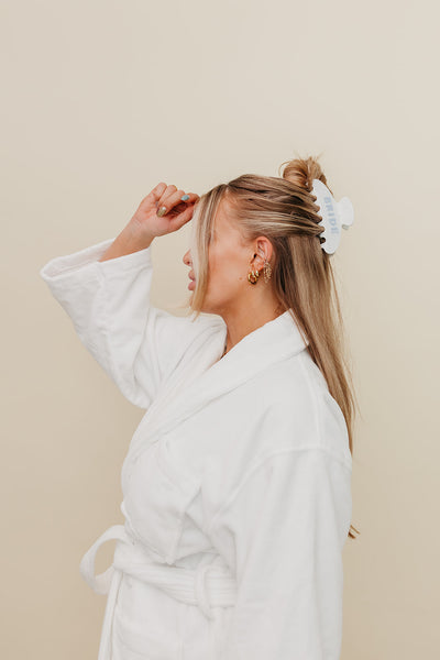 Woman in a white robe adjusting her hair against a beige background