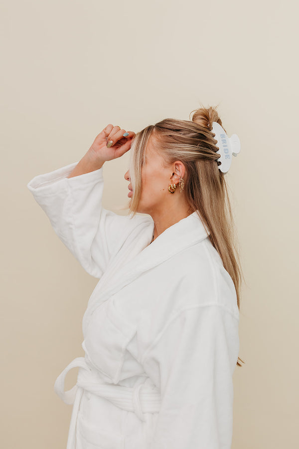 Woman in a white robe adjusting her hair against a beige background