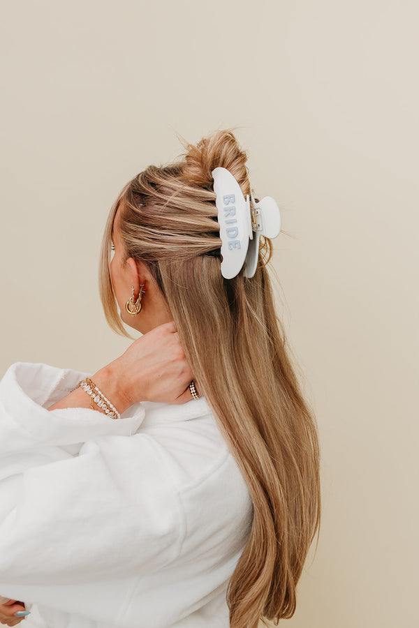 Person with long blonde hair wearing a white bride clip against a beige background