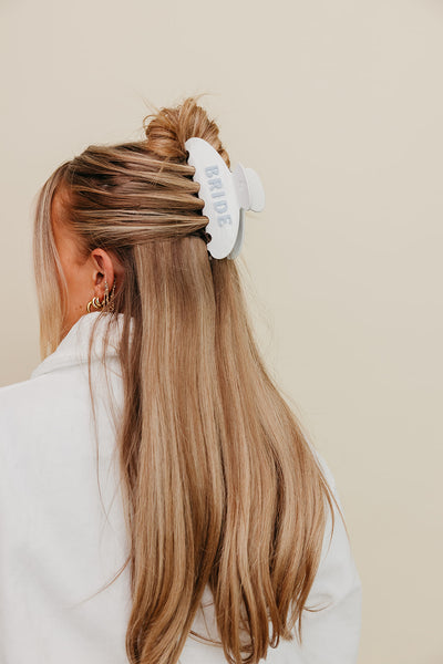 Person with long blonde hair wearing a white and blue bride claw on a beige background