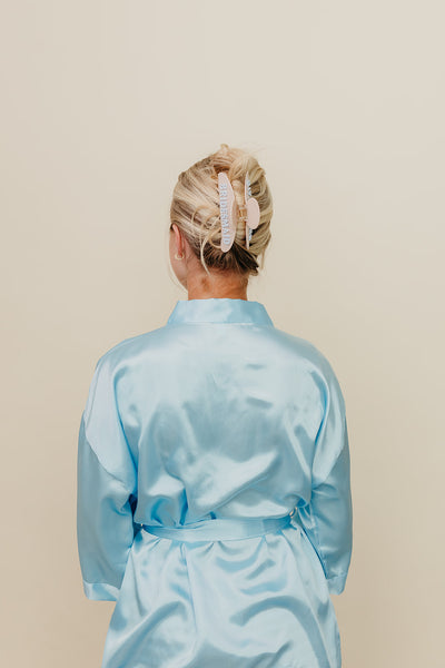 Person wearing a light blue satin robe with cream and blue bridesmaid claw against a beige background
