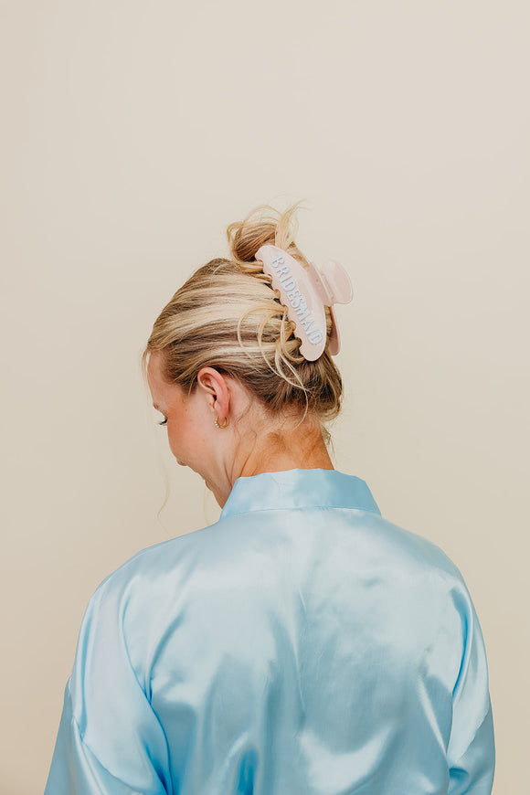 Person wearing a light blue satin robe and cream claw and blue claw clip with a neutral background