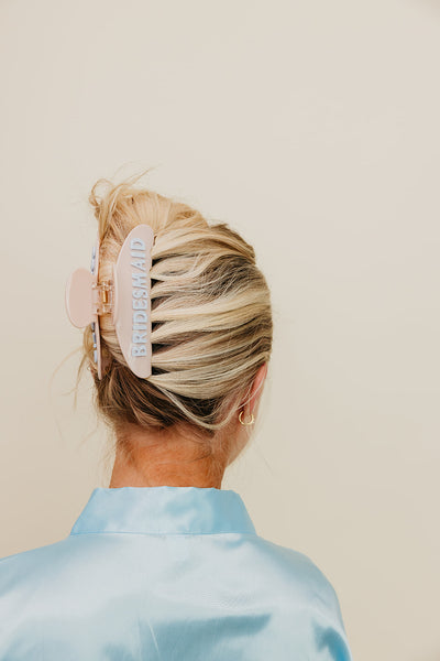Person with blonde hair styled in a cream and blue bridesmaid claw clip, against a plain background.