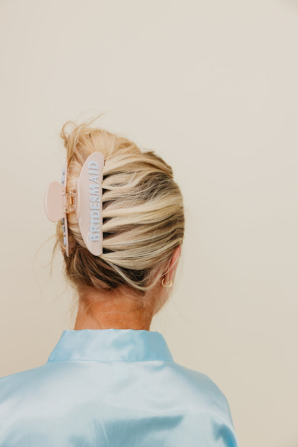Person with blonde hair styled in a cream and blue bridesmaid claw clip, against a plain background.