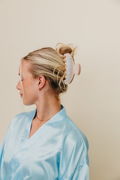 Woman wearing a blue satin robe with a bridesmaid claw on a beige background