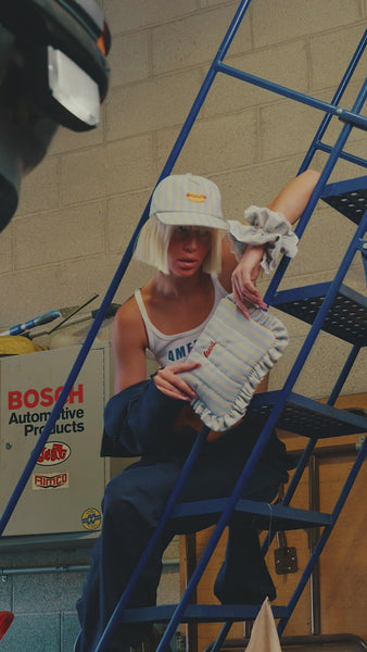 video of a girl wearing a blue and white striped baseball cap with a hot dog embroidered on the front,  with a matching blue and white striped scrunchie, and blue and white striped cosmetic bag